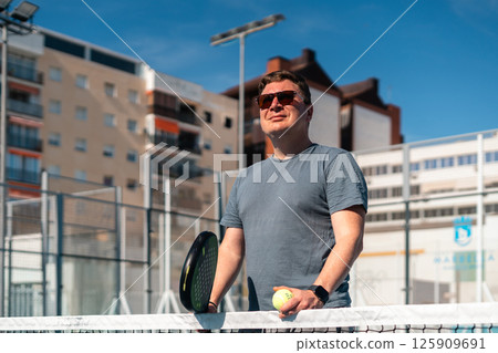 Smiling man enjoys sunny day on outdoor tennis court. Smiling man enjoys sunny day on outdoor tennis court. 125909691