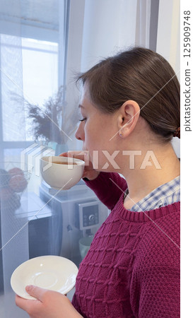 Portrait of joyful young woman enjoying a cup of tea at home. Excited woman wearing spectacles and sweater and laughing in an autumn day. Portrait of joyful young woman enjoying a cup of tea at home. Excited woman wearing spectacles and sweater and laughing in an autumn day. 125909748