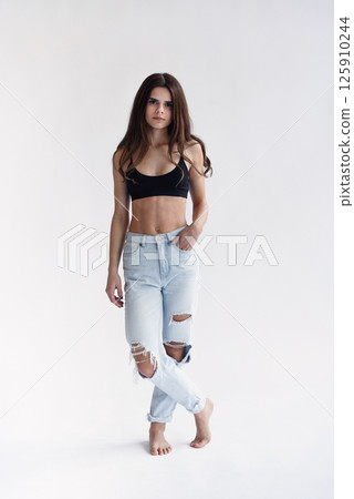 Charming skinny beautiful girl with perfect abs in jeans and black top isolated on light background 125910244