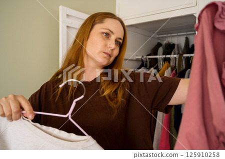 Woman choosing clothes from her closet, overwhelming amount of clothing Woman choosing clothes from her closet, overwhelming amount of clothing 125910258
