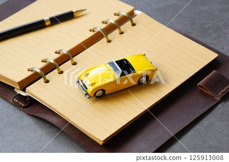 An image of planning a road trip with a miniature car, a ring-type system organizer, and a pen 125913008