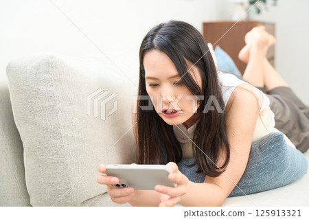 Woman looking at smartphone while lying down. Surprised. Surprised. Woman looking at smartphone while lying down. Surprised. Surprised. 125913321