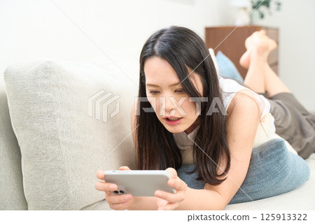 Woman looking at smartphone while lying down. Surprised. Surprised. 125913322