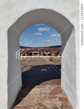 view wooden houses through an archway against clear blue sky on sunny day in rural landscape. 125914872