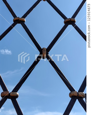 metal stylish sturdy lattice against bright blue sky with wispy clouds in afternoon. closeup. 125914873