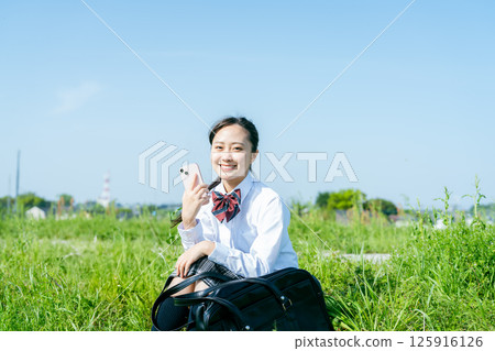 藍天下拿著智慧型手機的高中女生 125916126