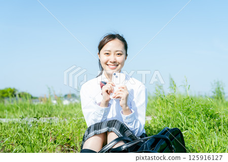 藍天下拿著智慧型手機的高中女生 125916127
