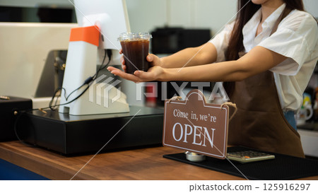 Coffee Business Concept Beautiful lady smiling at camera offers disposable take away ice coffee at the coffee shop 125916297