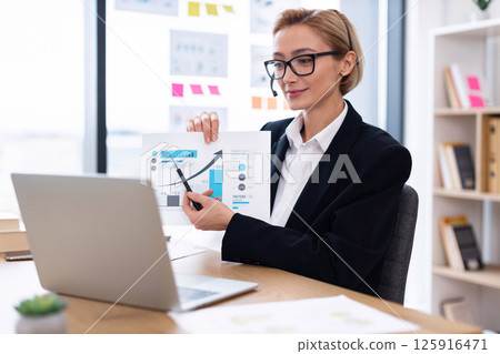 Businesswoman in thirties presenting financial graphs during online meeting using laptop, showcasing growth data. 125916471
