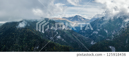 A breathtaking panorama of a mountainous landscape shrouded in mist. Lush greenery slopes into misty valleys beneath a dynamic sky, creating a serene yet dramatic view. Panorama of mountain range 125918436