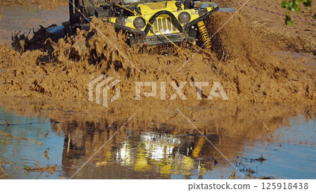 A yellow off-road vehicle rushes through a deep mud hole. The vehicle raises a large cloud of mud and water. There is a beautiful reflection of the SUV in the water. Extreme racing A yellow off-road vehicle rushes through a deep mud hole. The vehicle raises a large cloud of mud and water. There is a beautiful reflection of the SUV in the water. Extreme racing 125918438