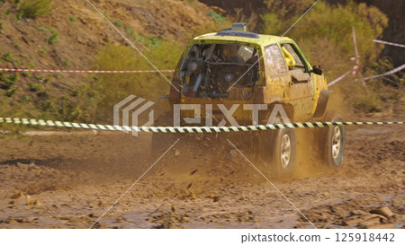 SUV racing on the mud. A yellow off-road vehicle is racing on a muddy highway. The car raises a cloud of splashes and mud, racing through difficult terrain 125918442