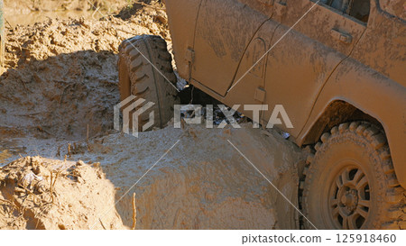 A muddy off-roader sat on the bottom on a complicated racing obstacle course. Close-up of an SUV stuck in the mud. Tires with aggressive tread hanging in the air A muddy off-roader sat on the bottom on a complicated racing obstacle course. Close-up of an SUV stuck in the mud. Tires with aggressive tread hanging in the air 125918460