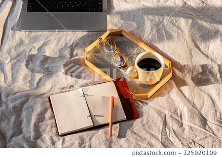 Setup with Laptop, Notebook, Pen, Glasses and Coffee Cup on Bed. Cozy Work from Home Concept. 125920109