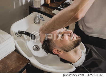 Young man with trendy haircut at barber shop. Barber washes customer head. Young man with trendy haircut at barber shop. Barber washes customer head. 125920165
