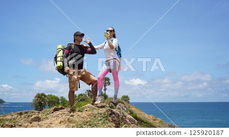 A young couple are hiking on a rugged rocky cliff that offers a view of the ocean 125920187