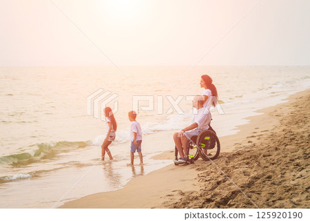 Disabled man in a wheelchair with his family on the beach. Disabled man in a wheelchair with his family on the beach. 125920190