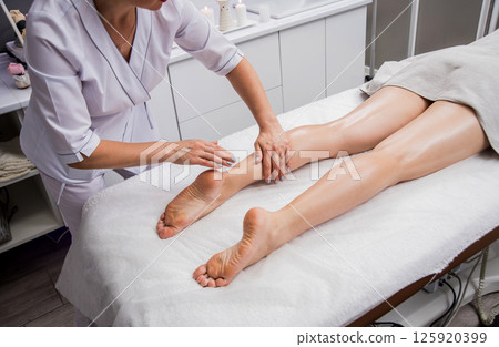 Beautiful young woman enjoying legs massage with oil in spa salon. Cosmetology Beautiful young woman enjoying legs massage with oil in spa salon. Cosmetology 125920399
