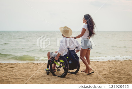 Disabled man in a wheelchair with his wife on the beach. 125920455