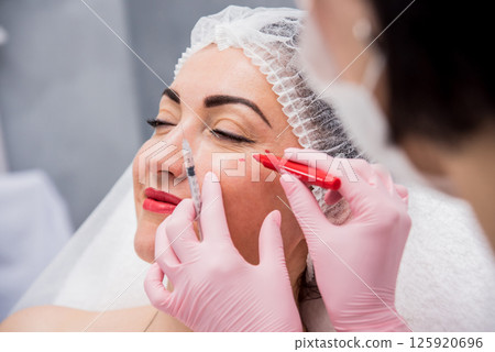 The doctor cosmetologist makes the facial injections procedure.  125920696