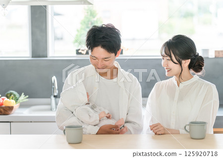 A young couple cradling their baby in the living room and dining room 125920718