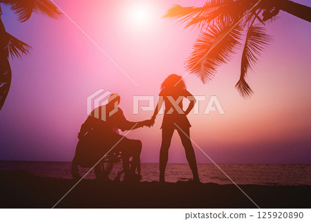 Disabled man in a wheelchair with his wife on the beach. Silhouettes at sunset 125920890
