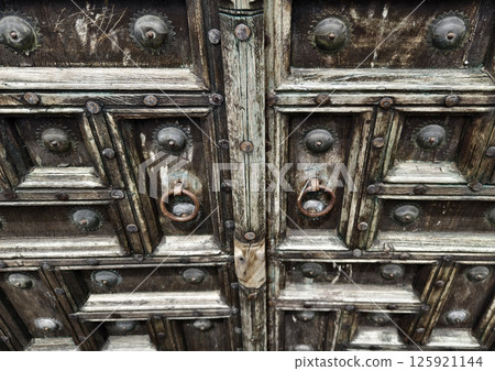 Detailed closeup of an antique wooden door decorated with elegant metal rings mounted on it. 125921144