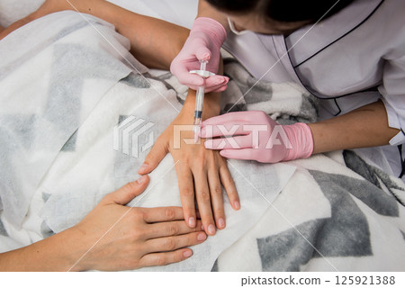 The doctor cosmetologist makes the arms injections procedure.  125921388