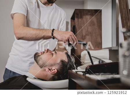 Young man with trendy haircut at barber shop. Barber washes customer head. 125921912