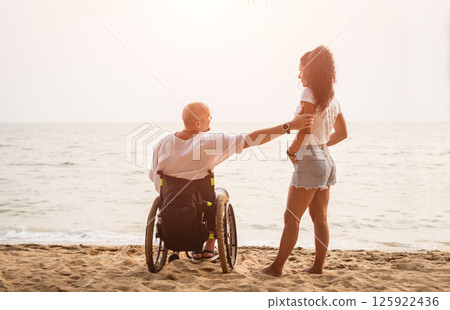 Disabled man in a wheelchair with his wife on the beach. Disabled man in a wheelchair with his wife on the beach. 125922436