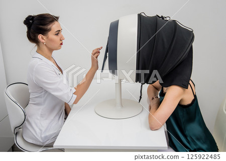 Face skin analyze system. Cosmetologist analyzing woman face.  125922485