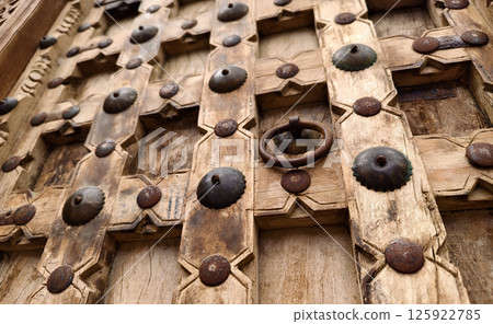 Detailed closeup of an antique wooden door decorated with elegant metal rings mounted on it. 125922785