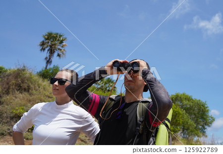 A man and a woman are intently looking through binoculars at something interesting in the distance A man and a woman are intently looking through binoculars at something interesting in the distance 125922789