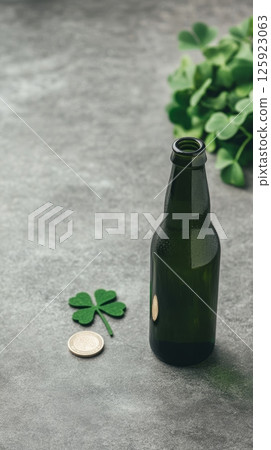 A dark green beer bottle sits on a gray surface next to a shamrock and a coin 125923063