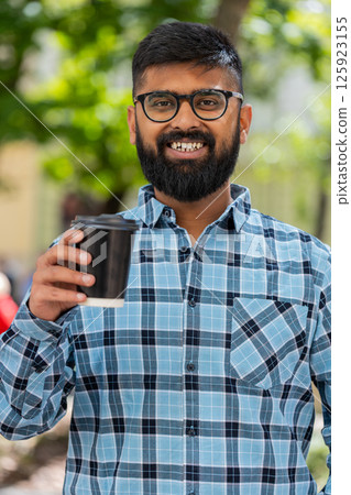 Happy Indian man enjoying drinking morning coffee hot drink, relaxing, taking a break on city street Happy Indian man enjoying drinking morning coffee hot drink, relaxing, taking a break on city street 125923155