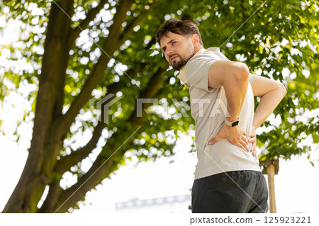 Young runner man suffering from back pain, sports injury, muscle spasm flank ache in city park Young runner man suffering from back pain, sports injury, muscle spasm flank ache in city park 125923221