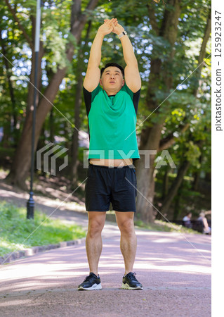 Japanese sporty healthy man athlete in park outdoors stretching hands stretch arms morning workout 125923247