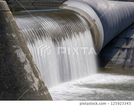 A rubberized fabric undulating weir with water flowing down 125923343