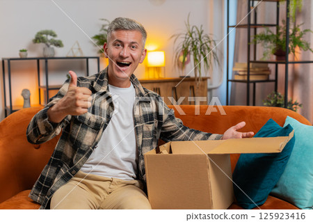 Happy customer man unpacking delivery parcel opening cardboard box receiving purchase gift at home Happy customer man unpacking delivery parcel opening cardboard box receiving purchase gift at home 125923416