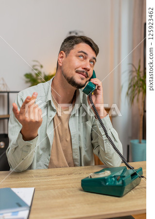 Caucasian man freelancer talking with client on retro old-fashioned wired telephone at table at home Caucasian man freelancer talking with client on retro old-fashioned wired telephone at table at home 125923462
