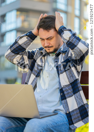 Caucasian mature man using laptop browsing loses lottery results, bad news sitting in city street 125923477