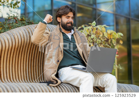 Overjoyed happy young man working on laptop netbook screaming in delight on bench in downtown city Overjoyed happy young man working on laptop netbook screaming in delight on bench in downtown city 125923529