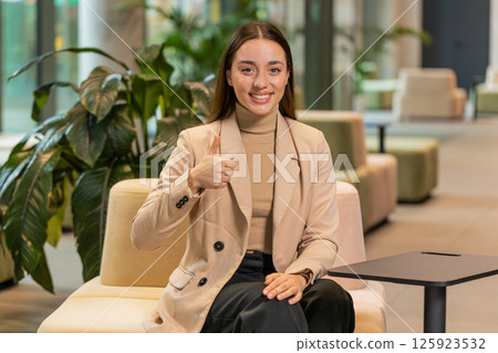 Portrait of smiling Caucasian young businesswoman girl in formal showing thumb up in hotel lobby Portrait of smiling Caucasian young businesswoman girl in formal showing thumb up in hotel lobby 125923532