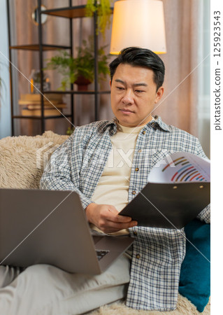 Stressed man freelancer feeling worried about financial problem doing paperwork sitting on sofa Stressed man freelancer feeling worried about financial problem doing paperwork sitting on sofa 125923543