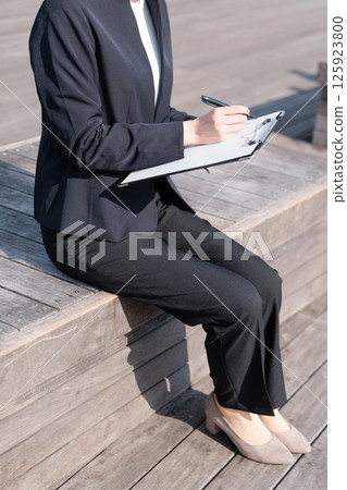A woman in a suit holding a clipboard outdoors A woman in a suit holding a clipboard outdoors 125923800