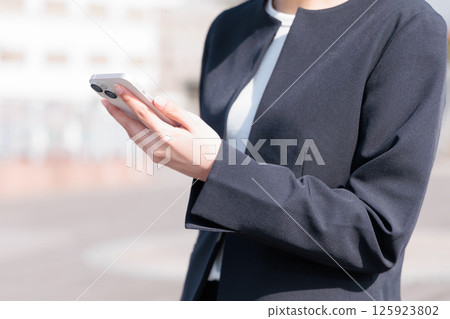 A young woman in a suit operating a smartphone outdoors 125923802