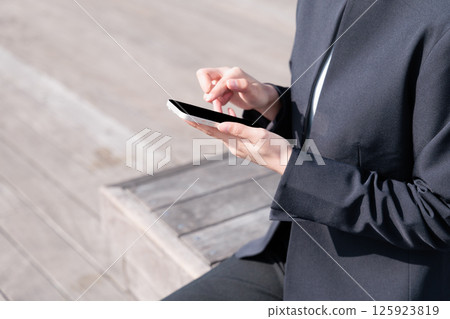 A young woman in a suit operating a smartphone outdoors 125923819