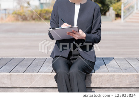 A woman in a suit holding a clipboard outdoors 125923824