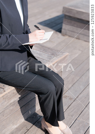 A young woman in a suit sitting on a bench outdoors and taking notes A young woman in a suit sitting on a bench outdoors and taking notes 125923833