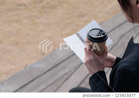 一位身著西裝的年輕女子一邊喝咖啡一邊看著記事本 125923877